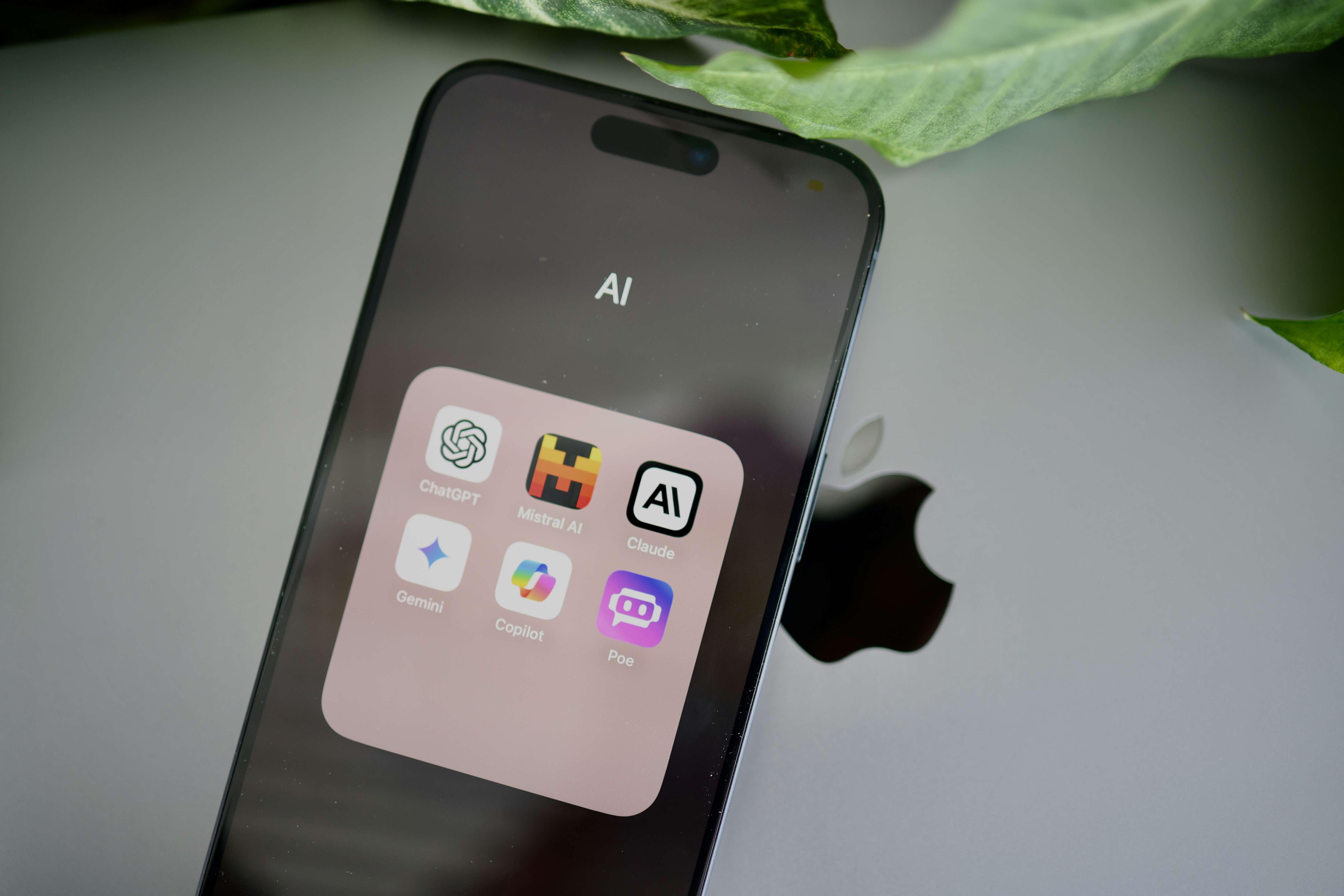 A smartphone depicts a folder with AI programs above an Apple laptop.