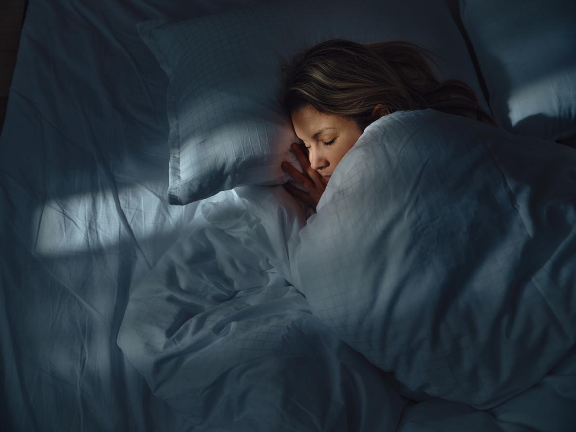 Overhead view of person sleeping in a bed with white sheets, pillows, and comforter.