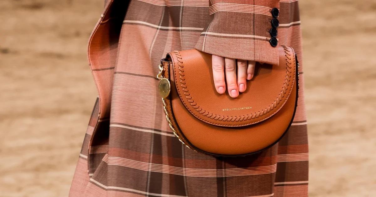 A person in a plaid coat holds a brown Stella McCartney bag