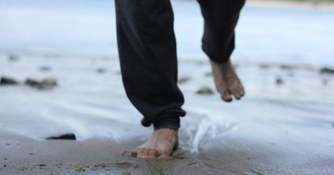 person in black pants walking barefoot on wet sand