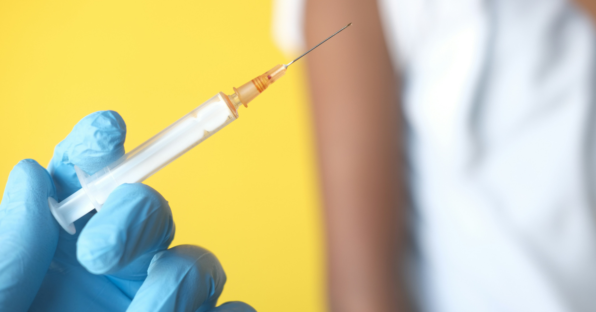 A blue gloved hand holds a vaccine dose