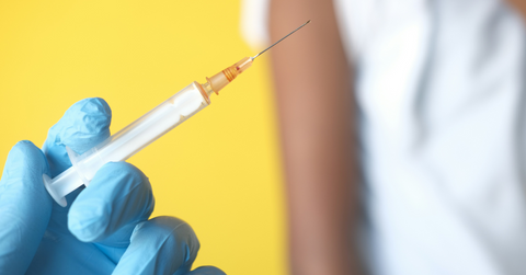 A blue gloved hand holds a vaccine dose