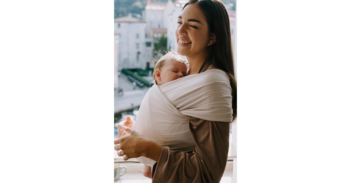 Smiling mom carrying sleeping baby in stone-colored sling.