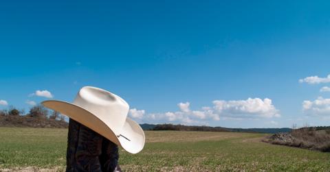 Cowboy boots in a field with a white cowboy hat on them.