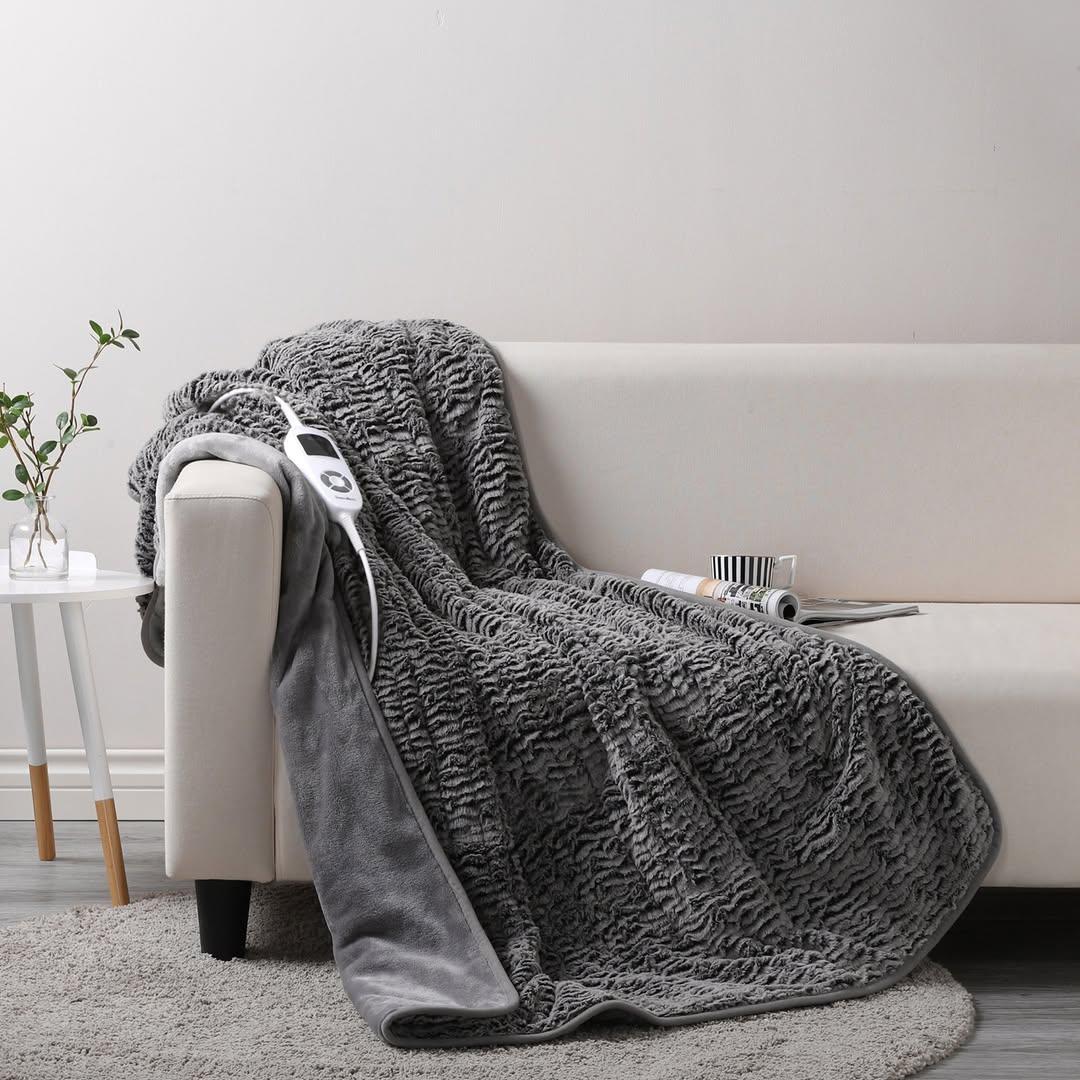 A gray plush electric throw blanket from the brand Temple & Webster is pictured on a cream colored couch.