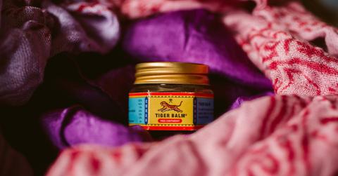 A jar of Tiger Balm is pictured on a pink and purple blanket.