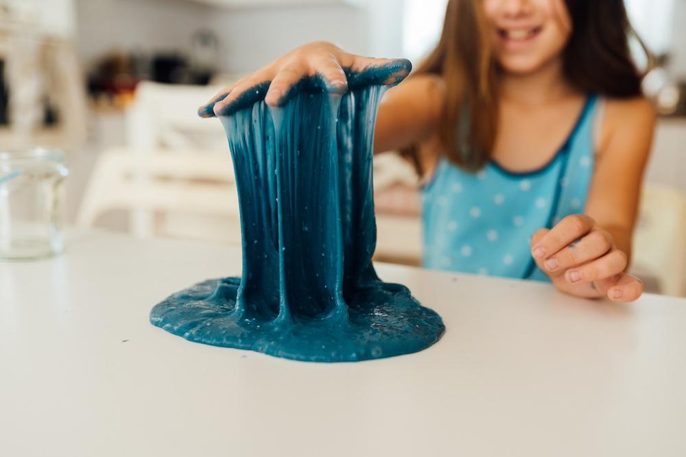 A kid wearing a blue tank top is playing with blue slime. 