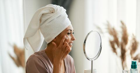 woman applying face cream and wearing a towel on her head