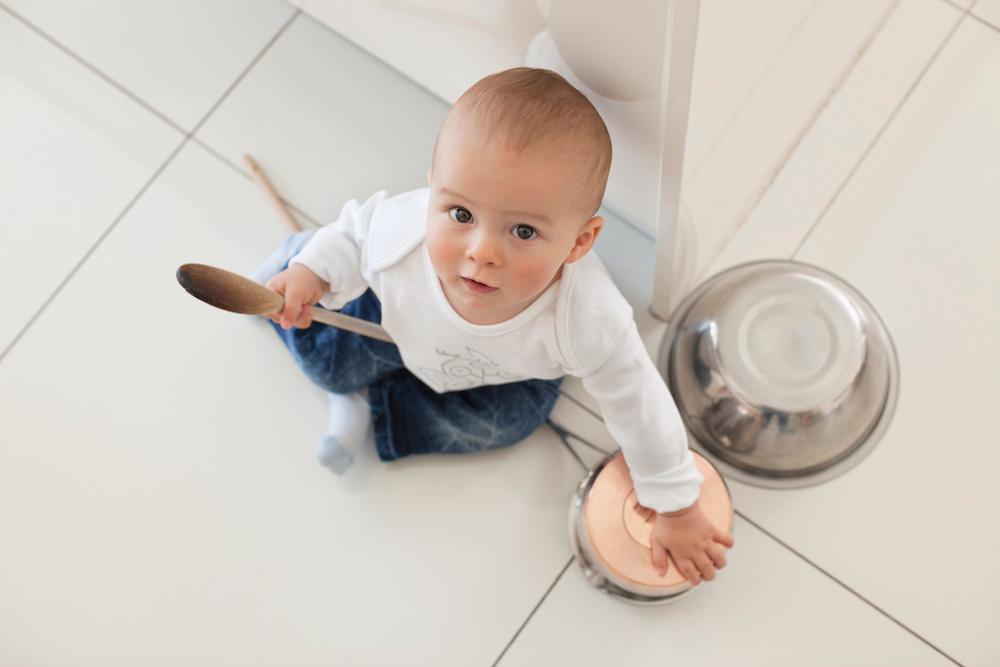 A baby sitting on the floor of a kitchen with pots. 