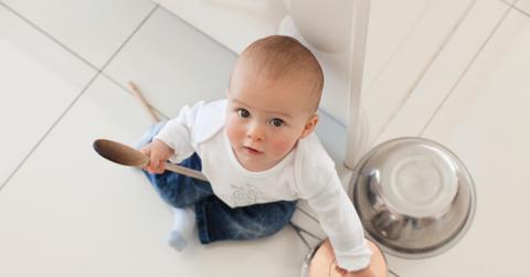 A baby sitting on the floor of a kitchen with pots.