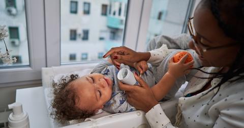 Baby lays on changing table and mother looks at him and holds jar of lotion