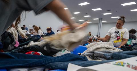 A low angle photo of people digging through blue bins at a Goodwill Outlet store, a blurry item of clothing flies across the top.