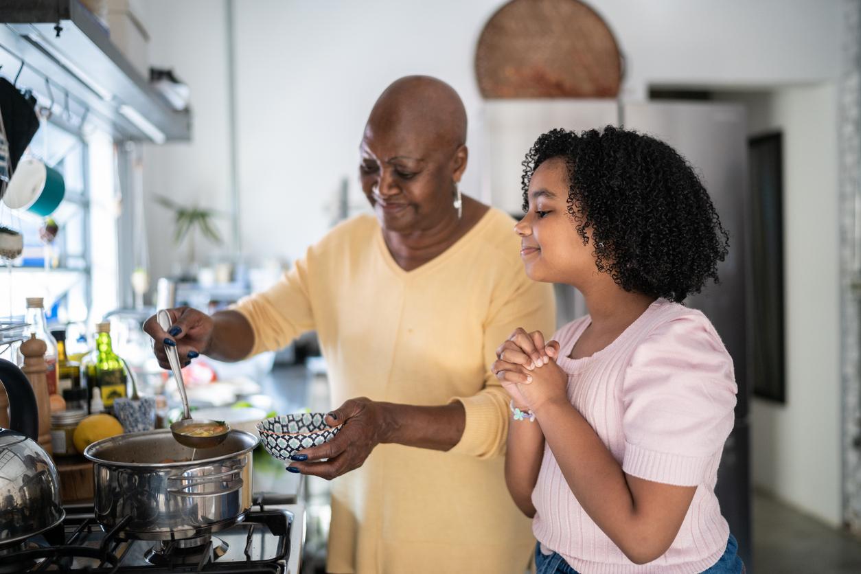 A smiling mother and daughter cook soup from a pot in their kitchen.