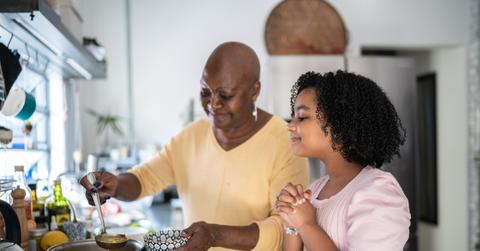 A smiling mother and daughter cook soup from a pot in their kitchen.