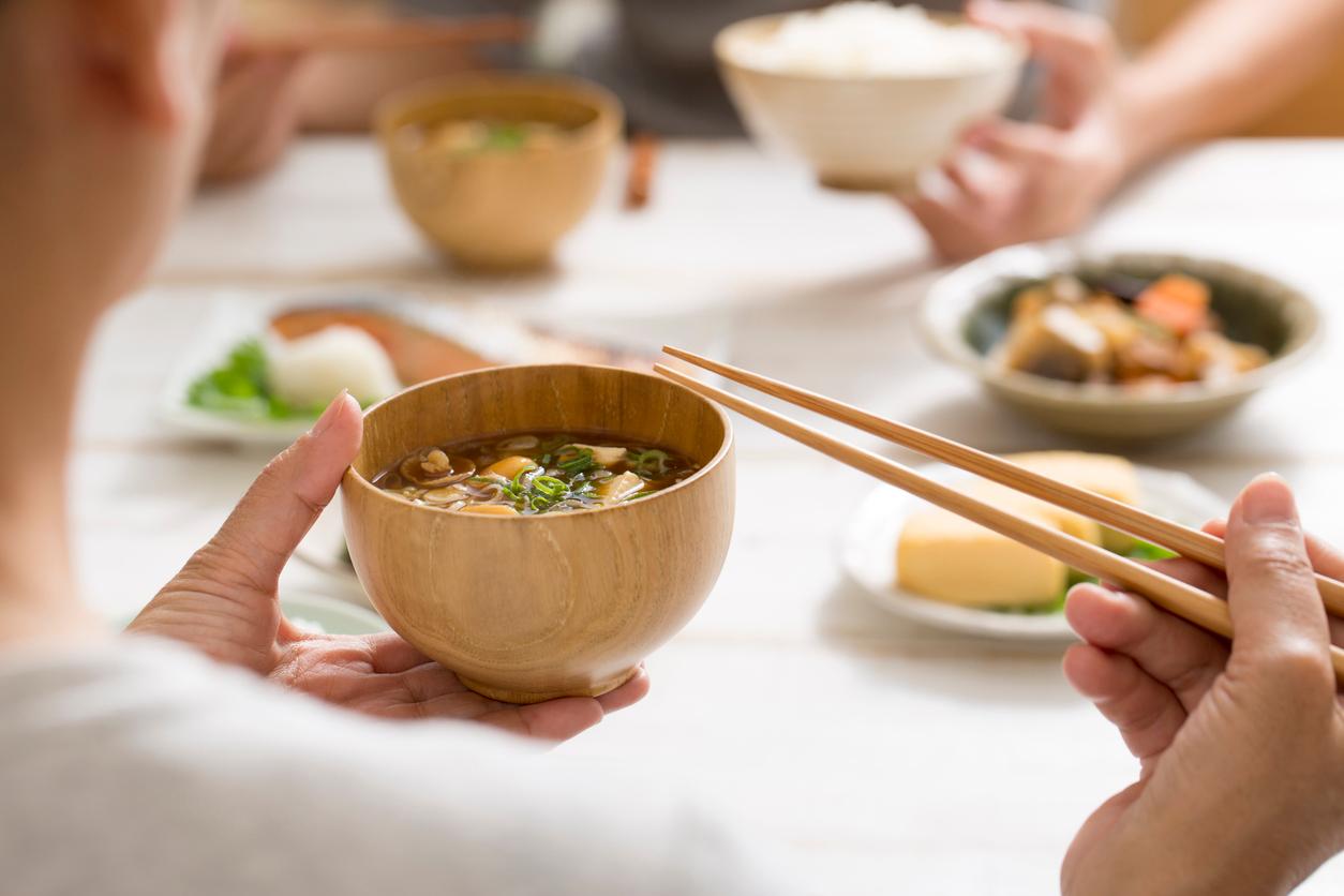 A family consumes Asian cuisine foods at a dinner table, with miso soup in a wooden bowl in the foreground.