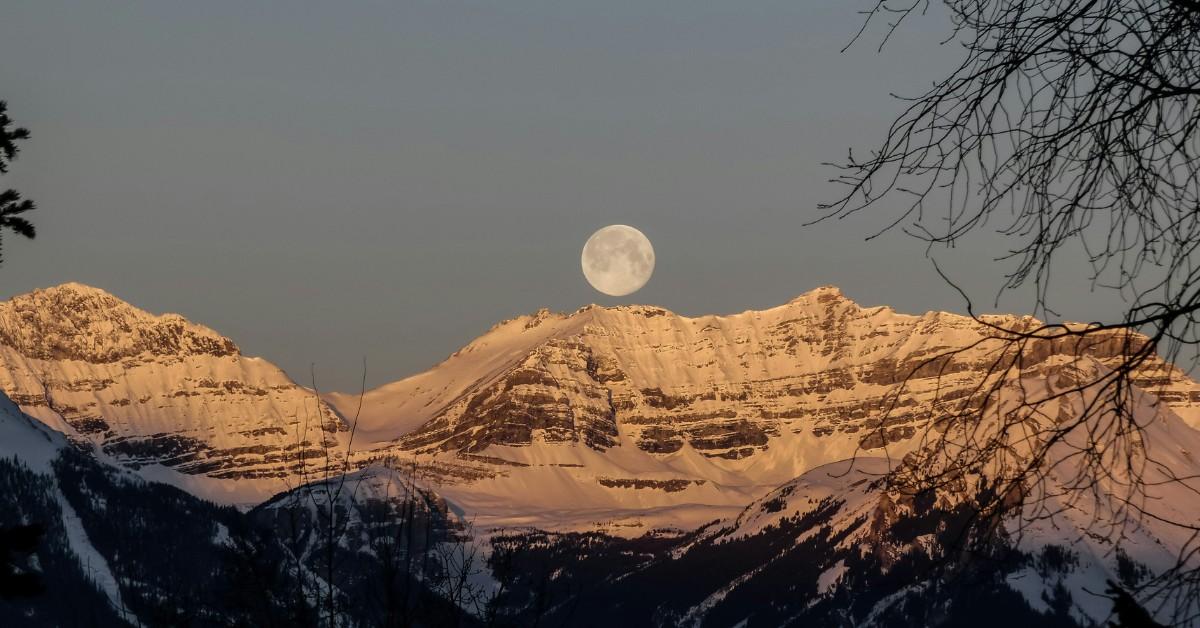 A full moon hangs over a snowy mountainside 