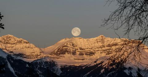 A full moon hangs over a snowy mountainside