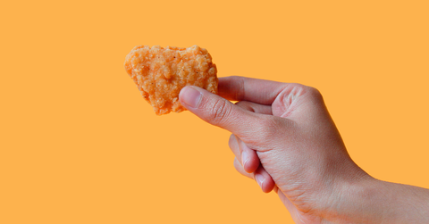 A hand holds a chicken nugget in front of an orange background