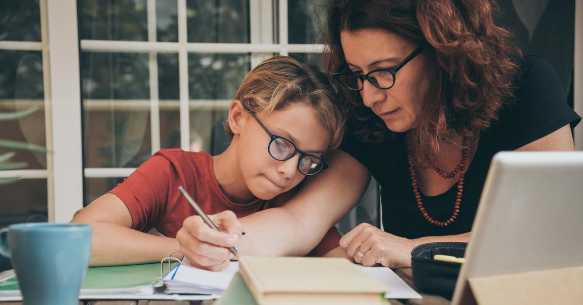 Student and his mother studying at home surrounded by notebooks, a laptop, and a blue mug.