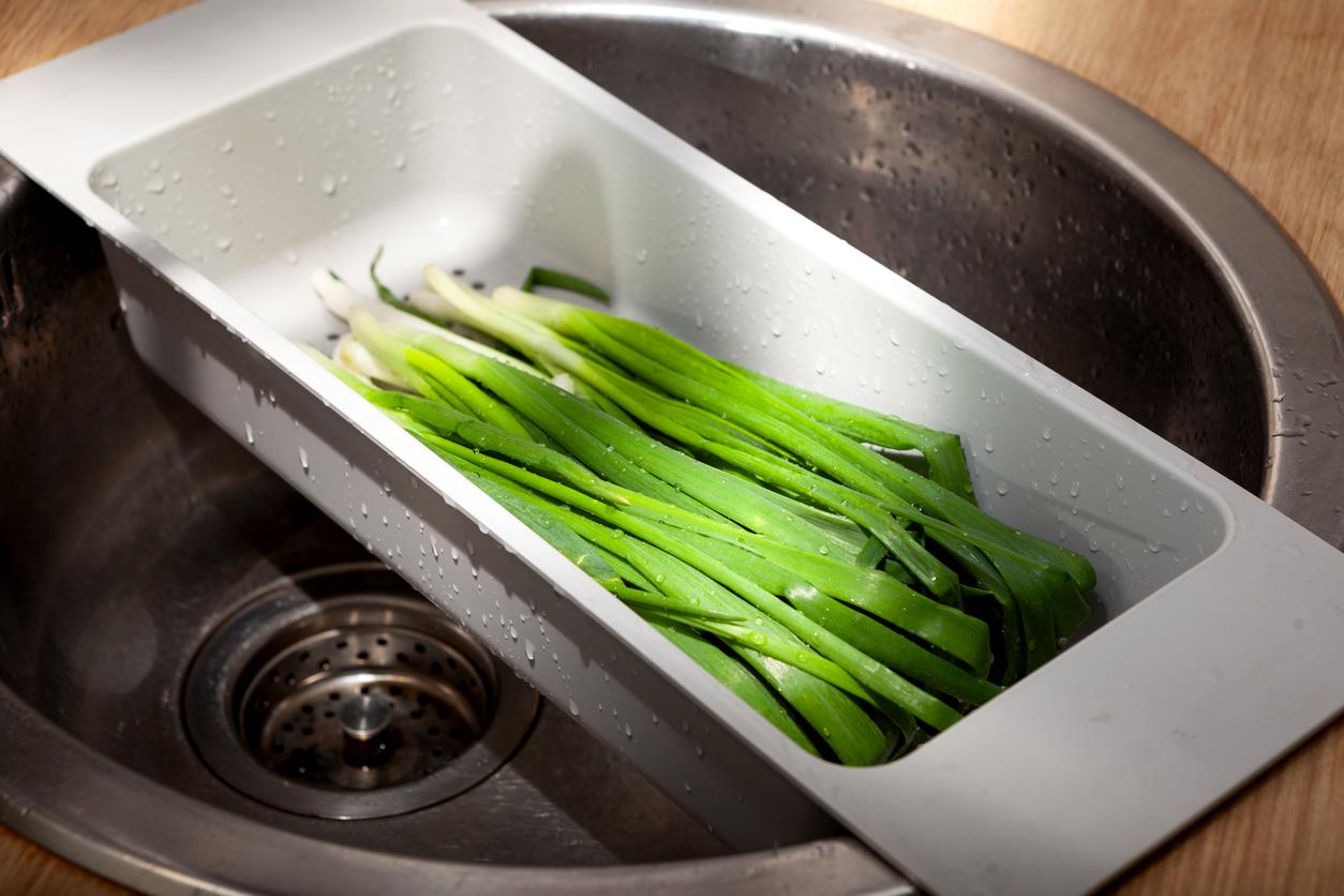 Green onions in a white rectangular strainer placed over the sink.