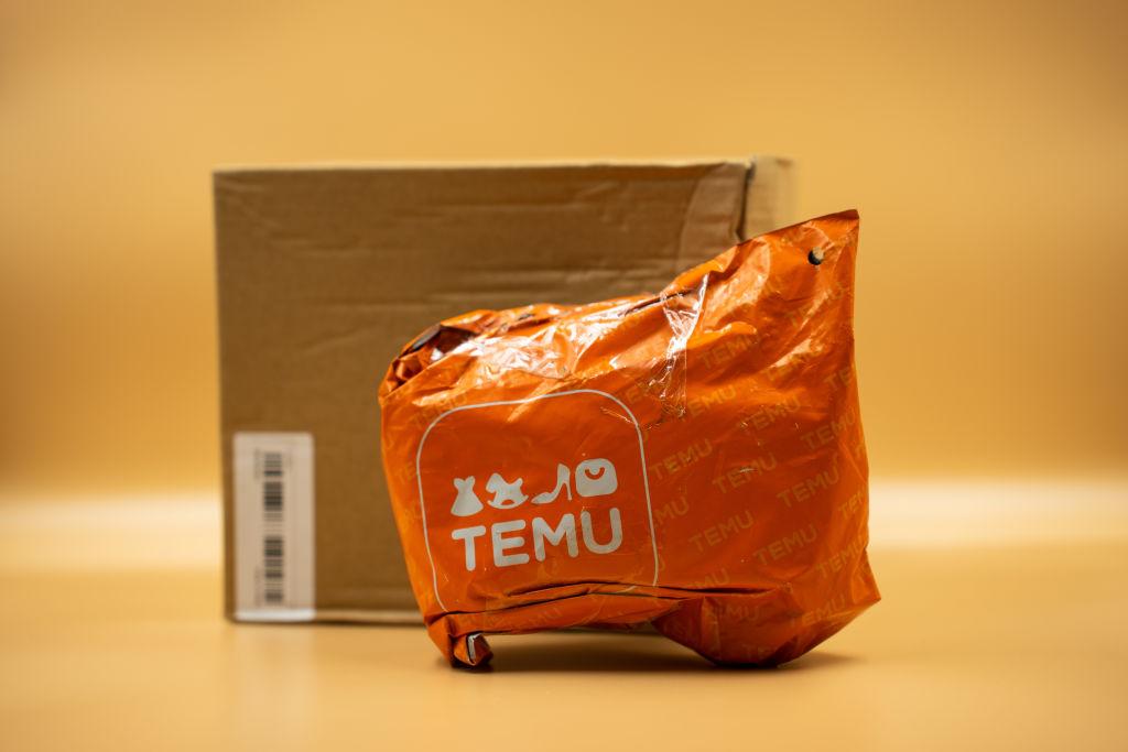 An orange, plastic Temu package in front of a cardboard box and light orange background.