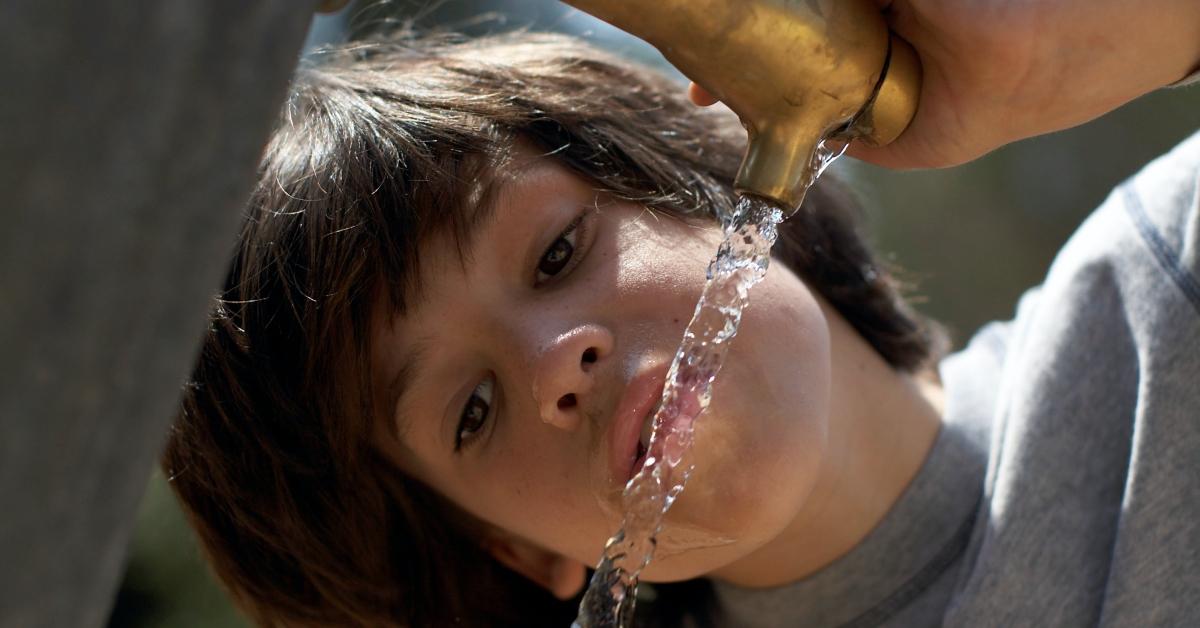 Boy drinking tap water from an outdoor faucet.