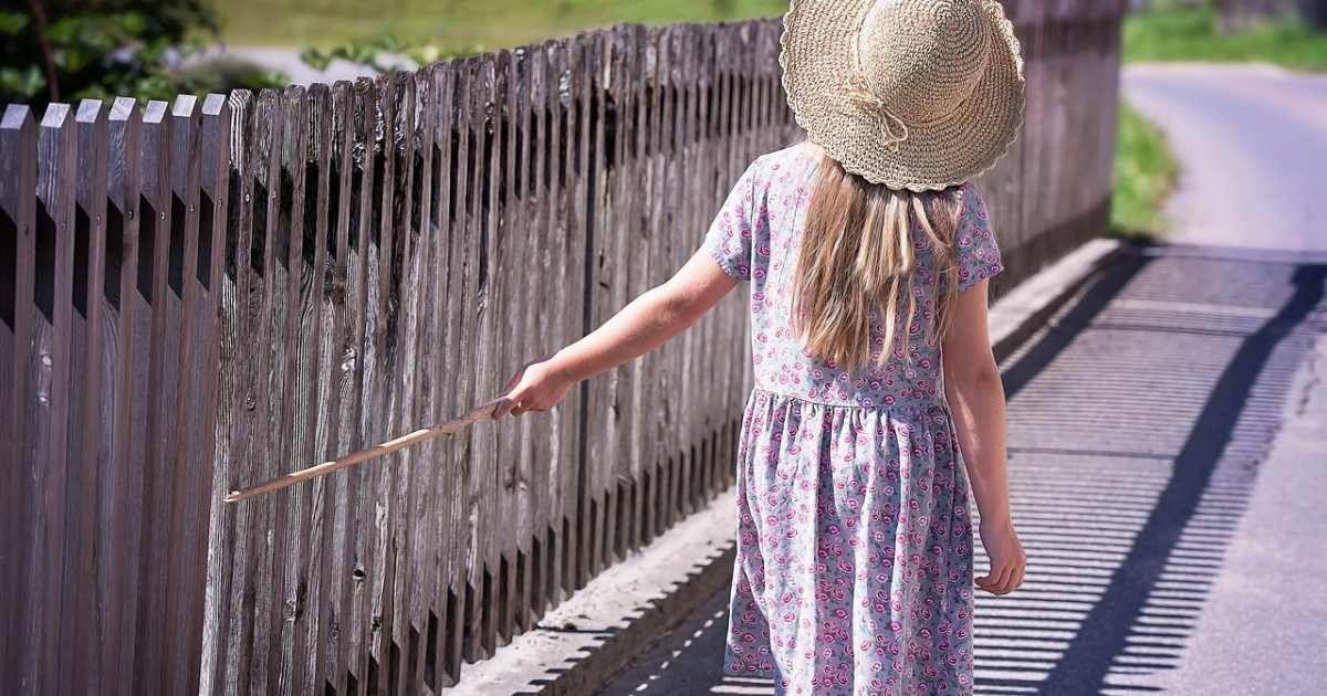 A little girl in a purple dress walking by a fence on a summer day. (Representative Cover Image Source: Pixabay | Pezibear)