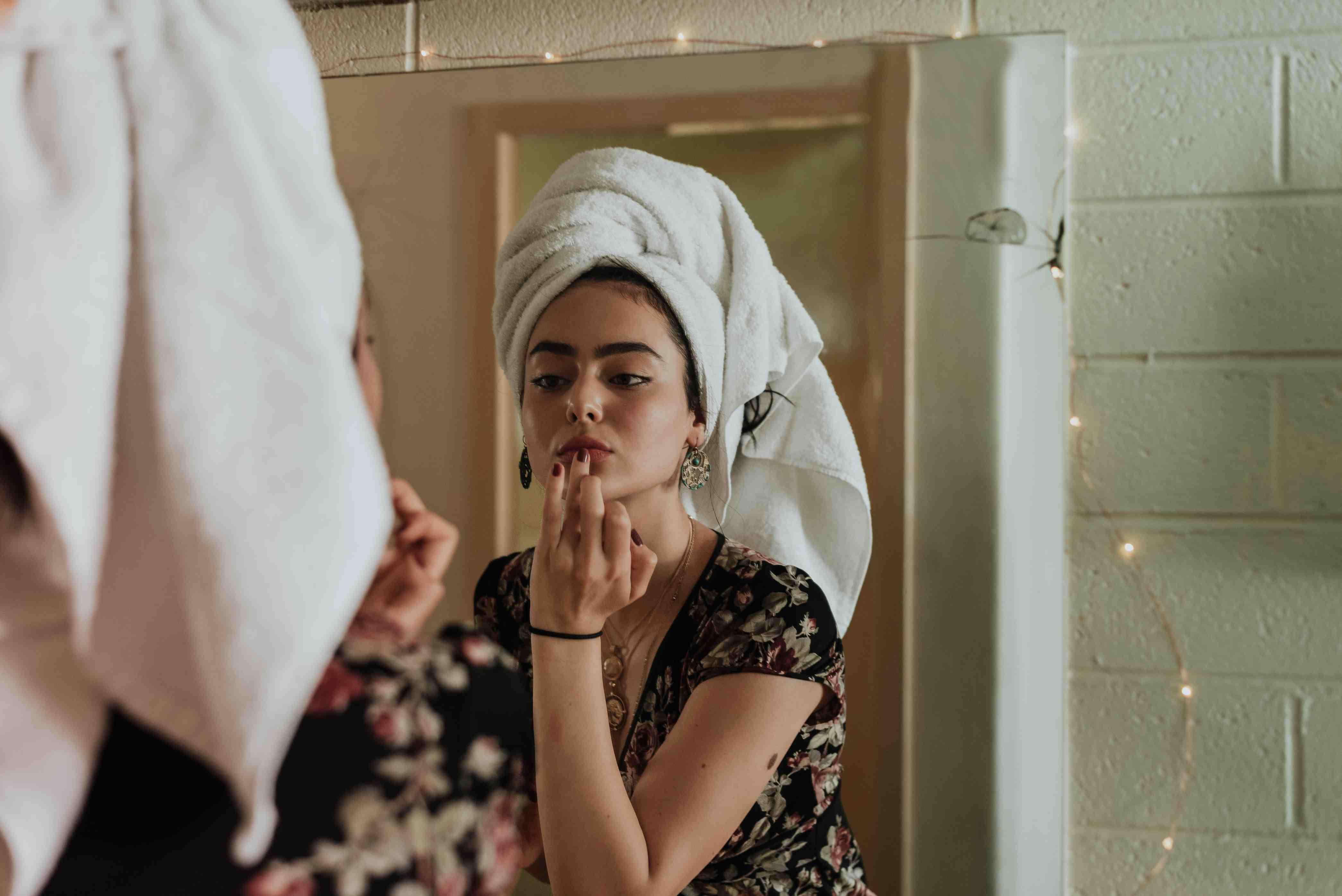A teen girl wearing a towel around her head applies serum to her face.
