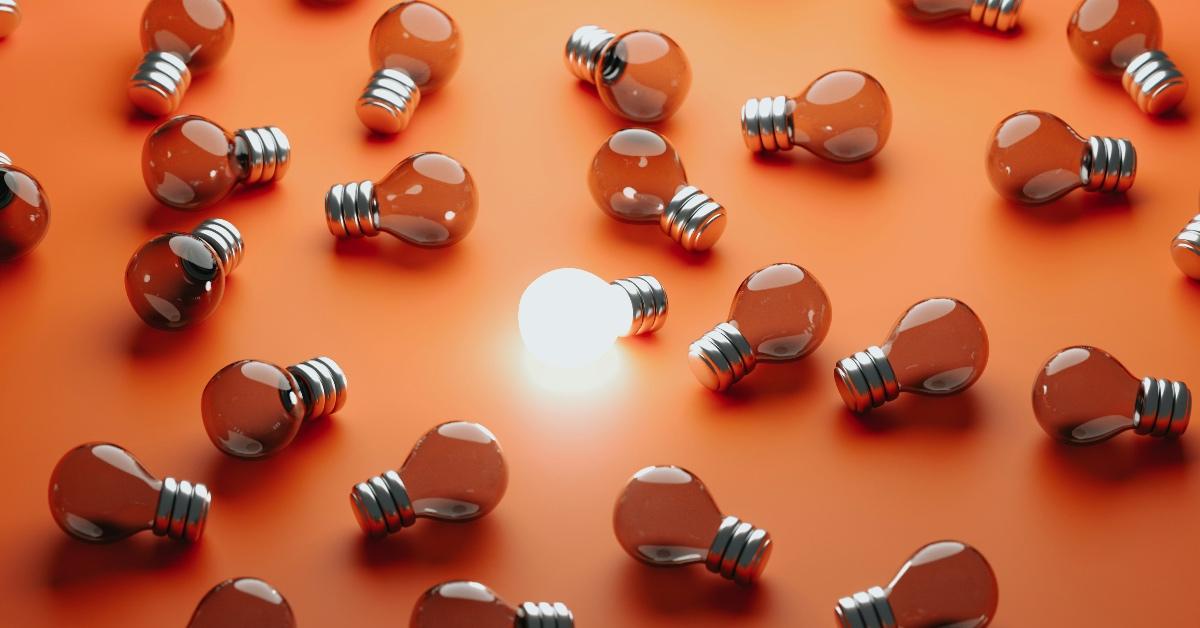 Lightbulbs scattered around an orange floor with one lightbulb in the center lit up. 