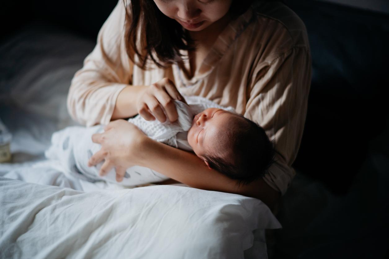 A mother wipes her baby's face with a homemade wipe while the baby is swaddled in a blanket.