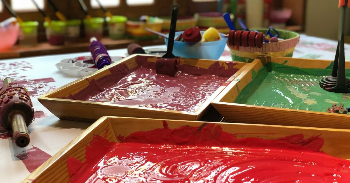 Three paint trays sit on a table filled with toddler-friendly painting supplies