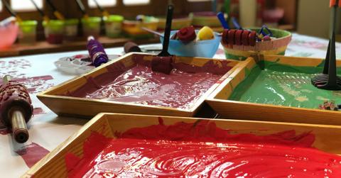 Three paint trays sit on a table filled with toddler-friendly painting supplies