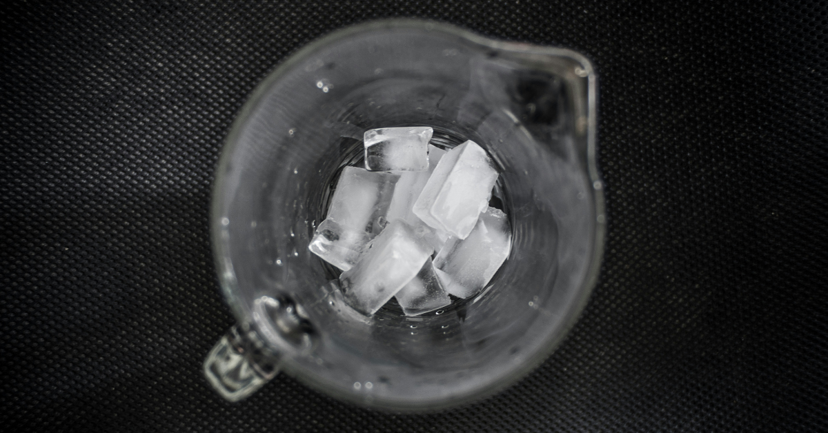 A pitcher with ice cubes covering the bottom sits on a black mat 