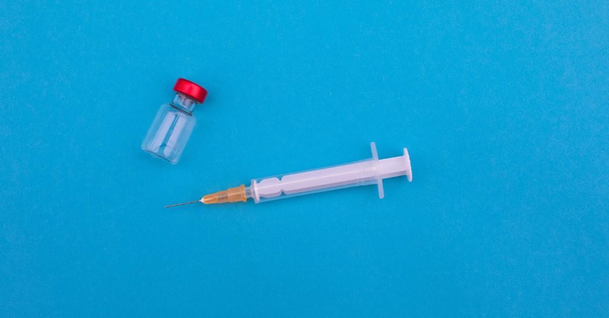 A medicine vile and a syringe sit on a blue background 