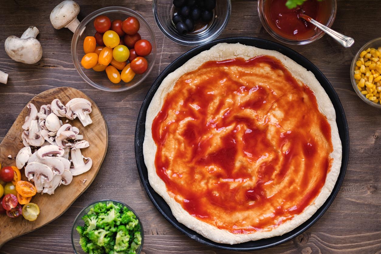 Pizza dough with sauce on it, surrounded by a variety of plant-based ingredients.