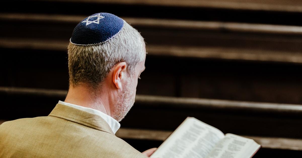 A man in a tan suit wears a kippah while reading religious text in a church. 