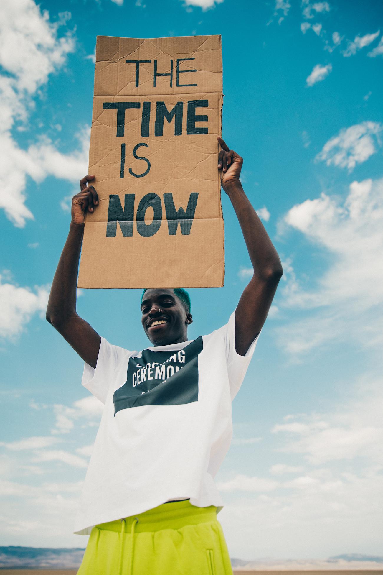 Person holds up poster saying "the time is now"