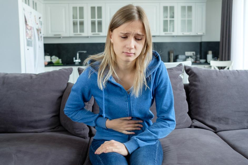 A young girl with blonde hair and a blue jacket holds her stomach in pain. 