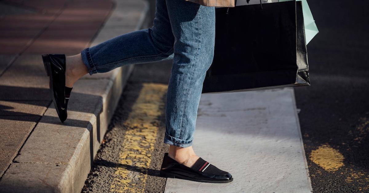 Legs of a woman in jeans and loafers walking with shopping bags