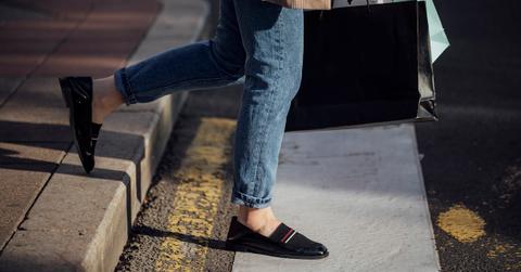Legs of a woman in jeans and loafers walking with shopping bags