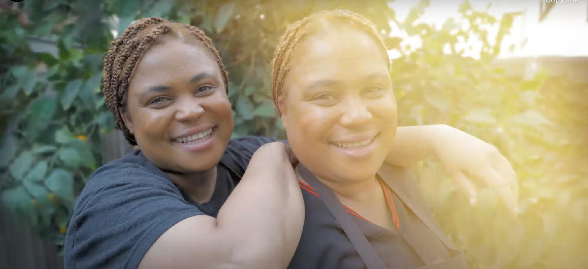 Twins Pam and Wendy pose together in black kitchen chef outfits in front of greenery in a mini-documentary about their food business.