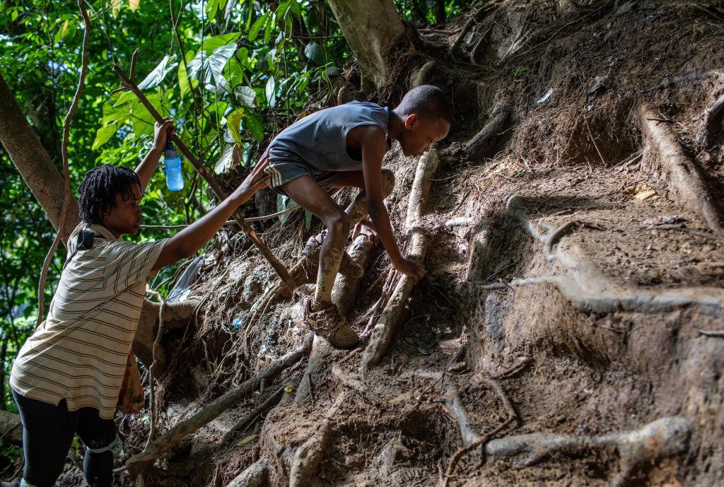 An older boy helping a younger child climb up a hill during their dangerous journey through the Darien Gap.