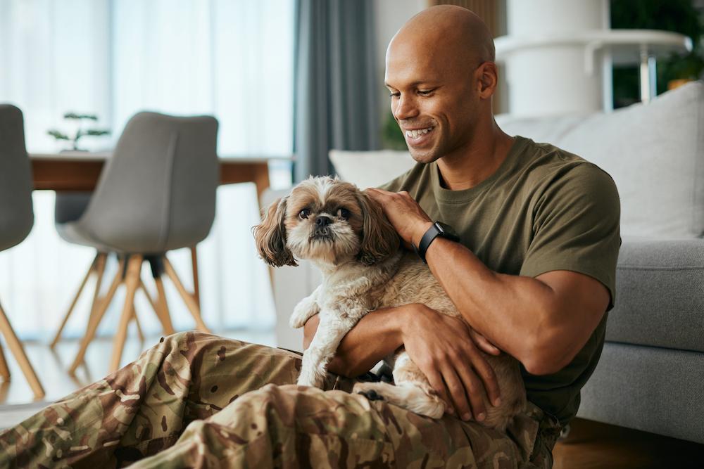 A man holding a Shih Tzu while sitting on the floor. 