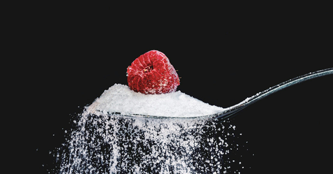 A raspberry sits on top of a spoonful of sugar