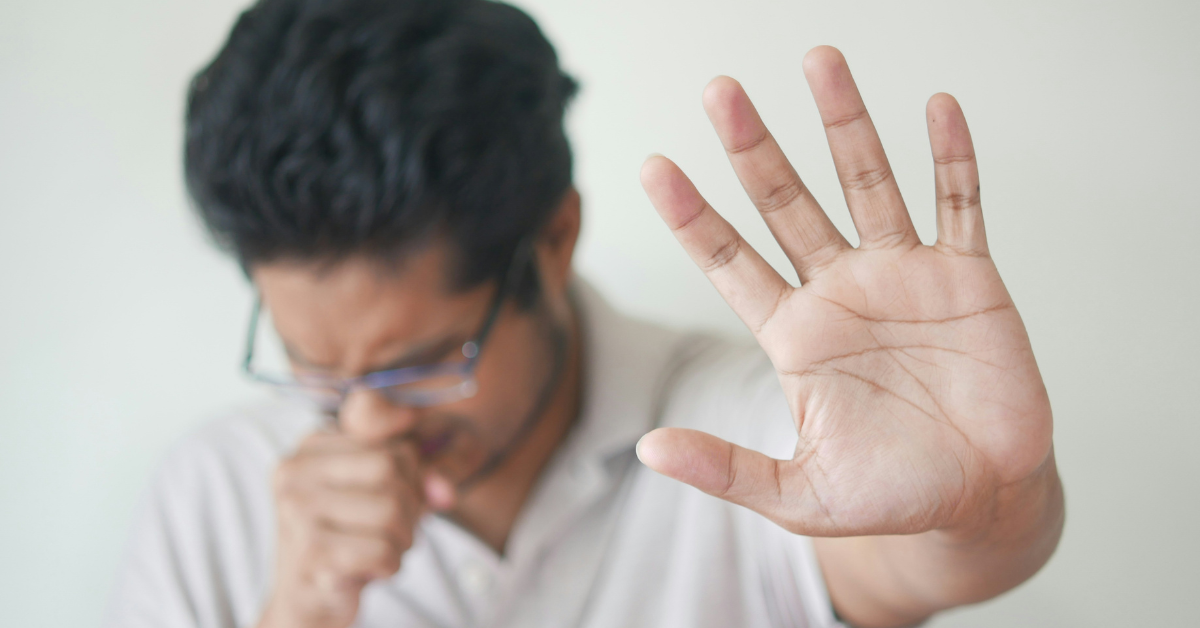 A man holds up a hand while sneezing