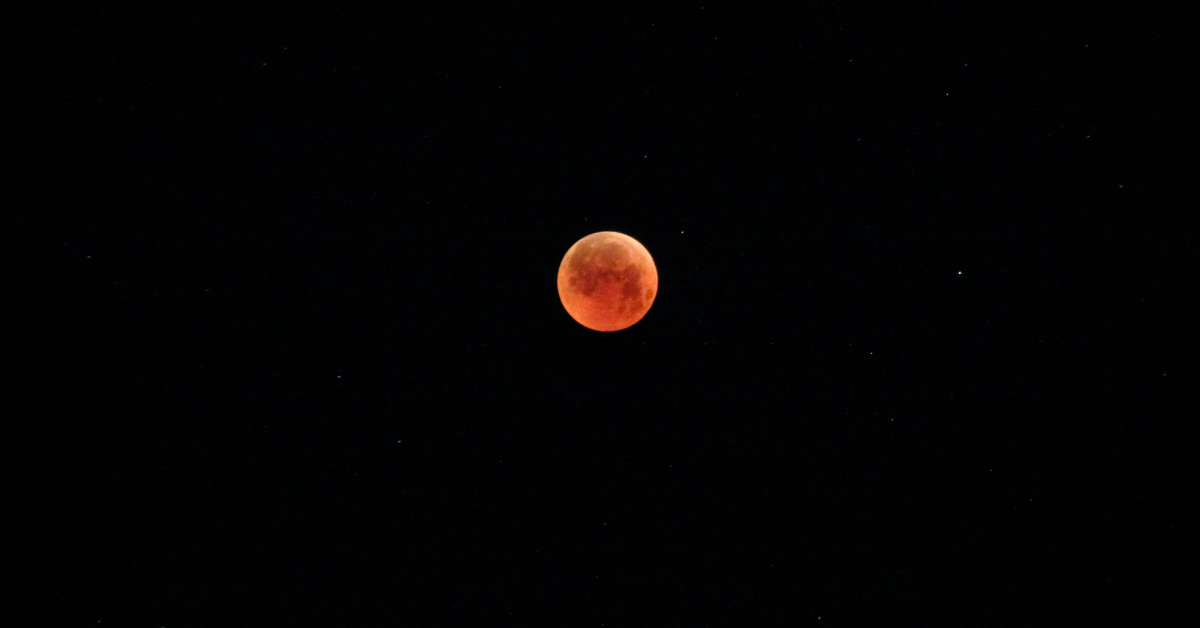 A red tinged moon sits in the night sky