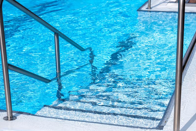 Metal railing and stairs leading into a chlorinated pool. 