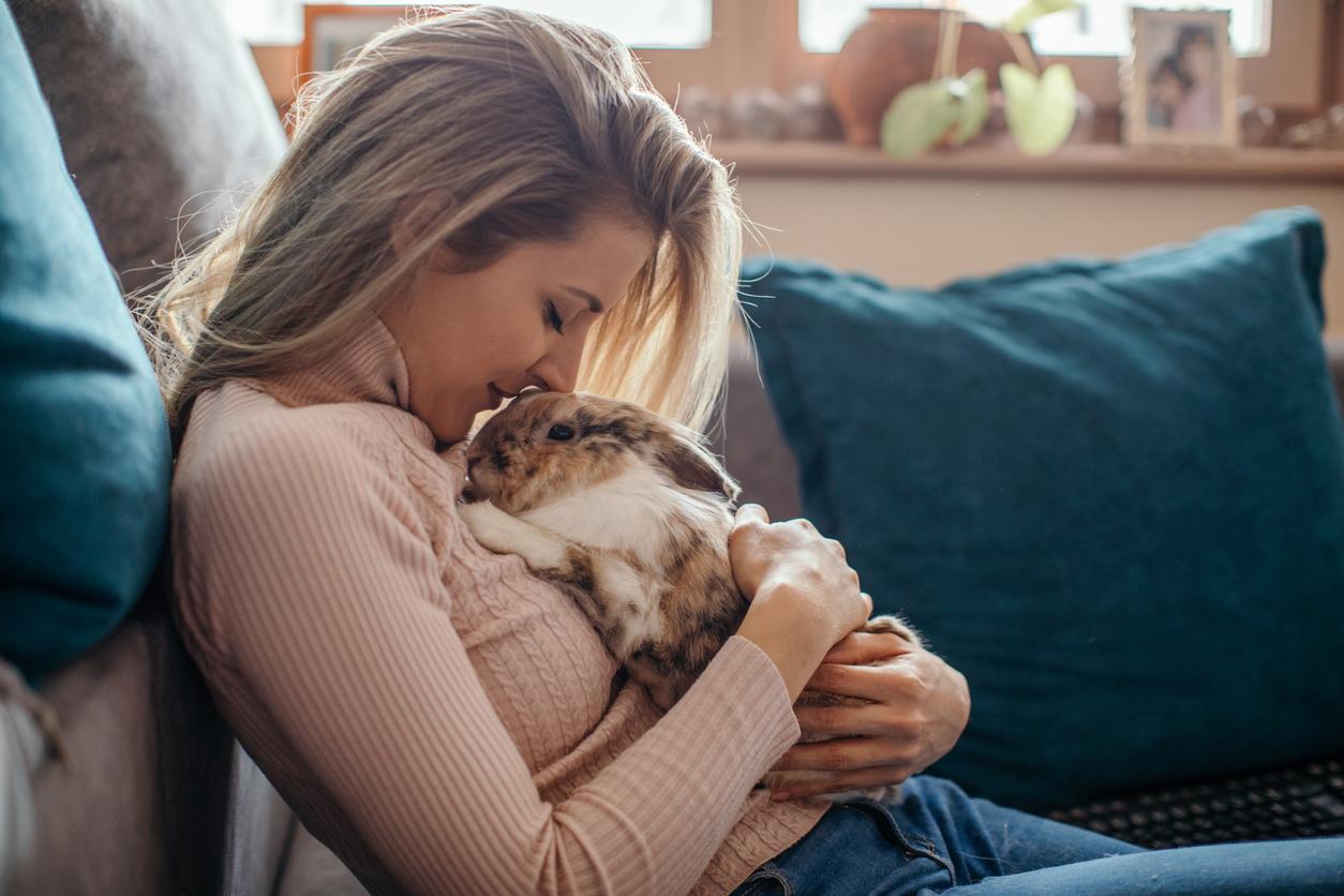 A woman smiles upon her companion rabbit while holding the rabbit in her arms as she leans back against her couch.