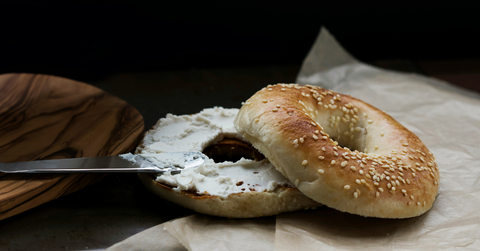 A knife spreads cream cheese over a bagel