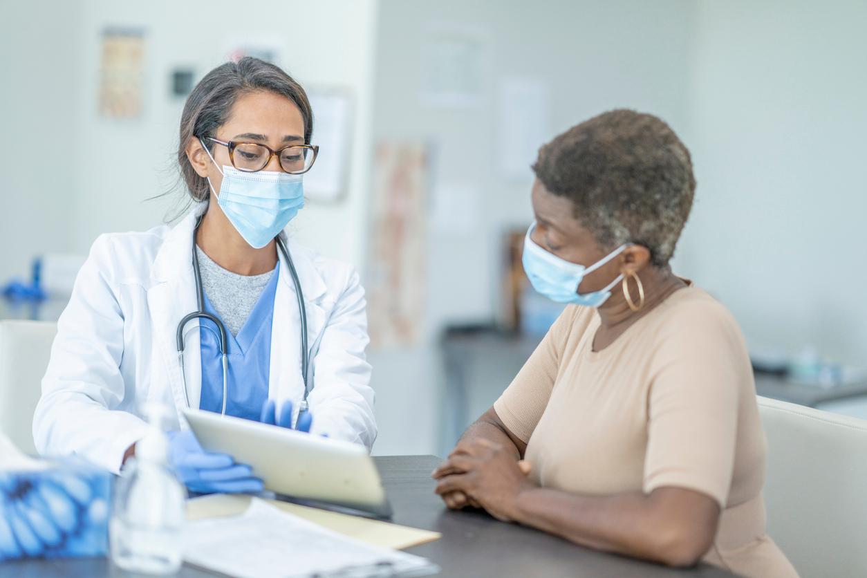 A medical doctor wearing a mask explains a chart to a patient wearing a mask.